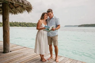 Couple en lune de miel lisant une brochure de voyage sur la terrasse d'un bungalow sur pilotis dans un lagon turquoise