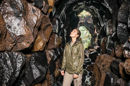 Femme explorant un tunnel de lave volcanique à La Réunion sous la pluie, activité géologique en intérieur