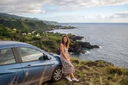 Jeune femme en robe fleurie et sneakers devant une voiture sur un sommet