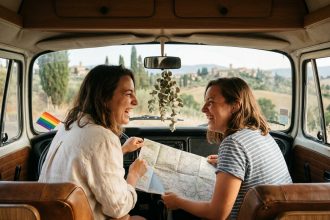 Deux femmes souriantes consultant une carte routière dans un van vintage lors d'un road trip LGBTQ+ en Europe