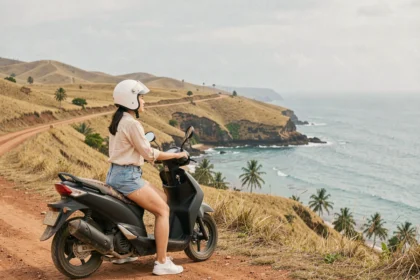 Jeune femme en scooter sur une route panoramique côtière à Kuta Lombok, avec vue sur la baie turquoise et les collines dorées